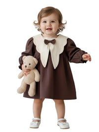 Thumbnail for Child wearing a brown dress with a white collar holding a teddy bear on a white background