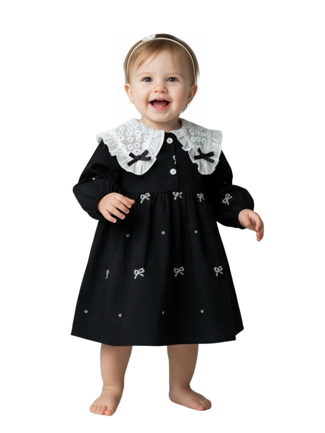 Baby wearing a black dress with white collar and bow details on a white background