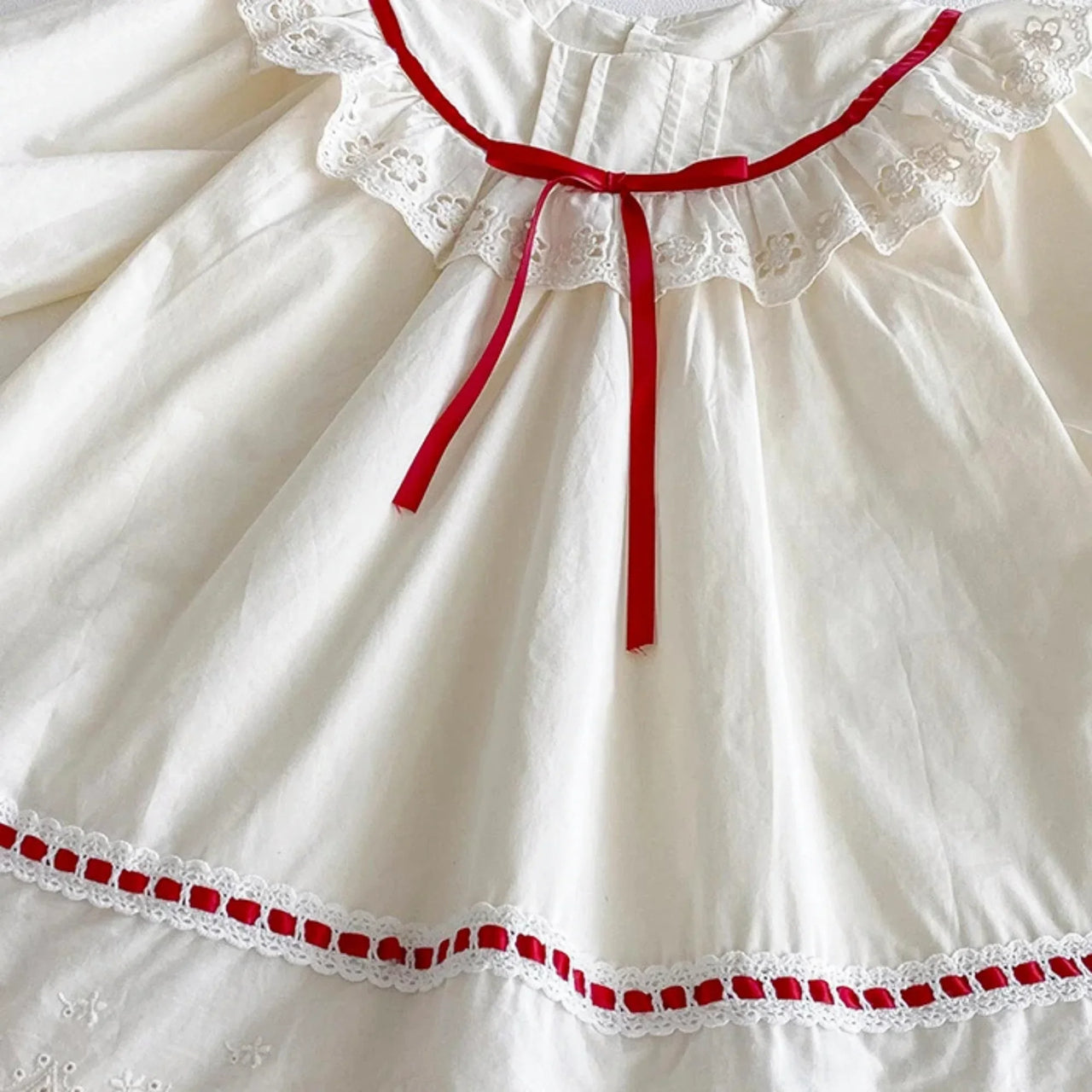 White dress with red trim and lace details on a white background