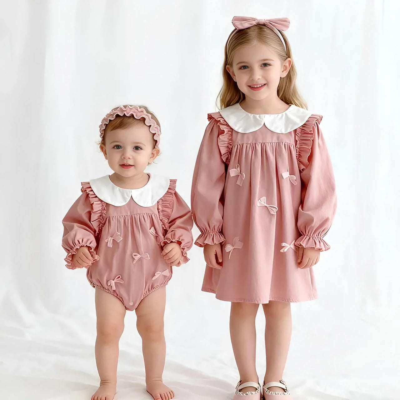 Two children wearing matching pink outfits with white collars on a white background