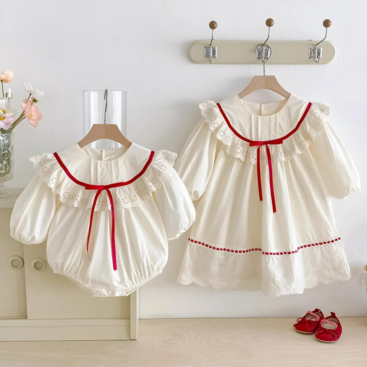 White baby dress with red trim on a hanger against a white wall.