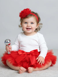 Thumbnail for Baby in a red tutu and headband holding a rattle on a light gray background