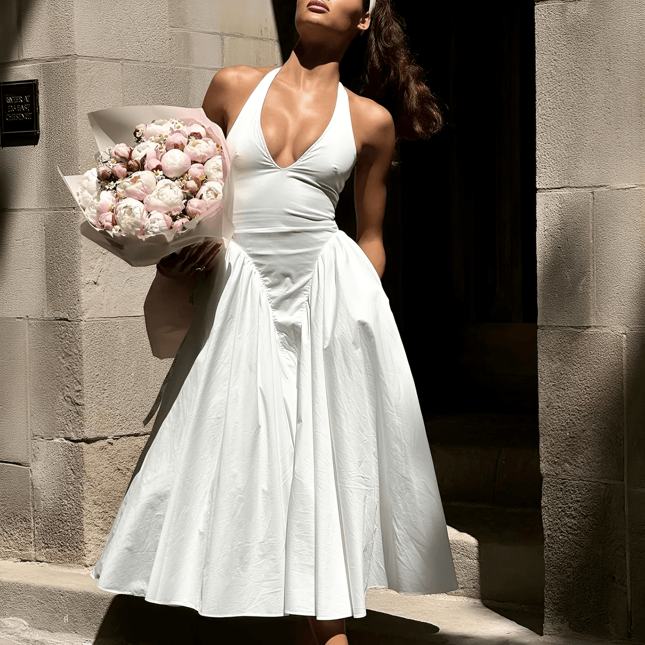 Woman in a white dress holding a bouquet of flowers against a stone wall.