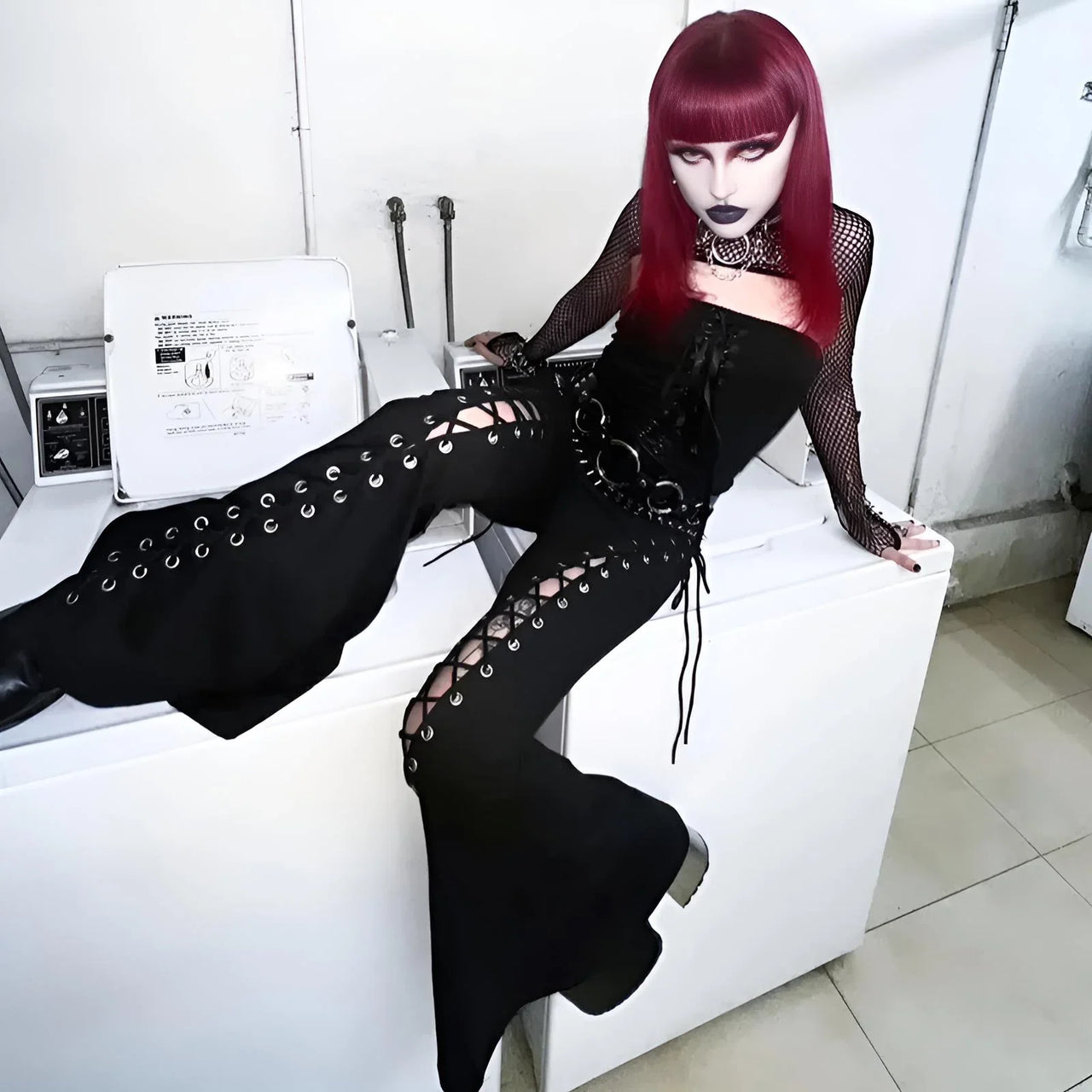 Person in black outfit with red hair sitting on a white surface in a room.