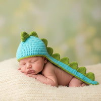 Thumbnail for Newborn baby wearing a dinosaur-themed crochet hat with a blurred green and brown background
