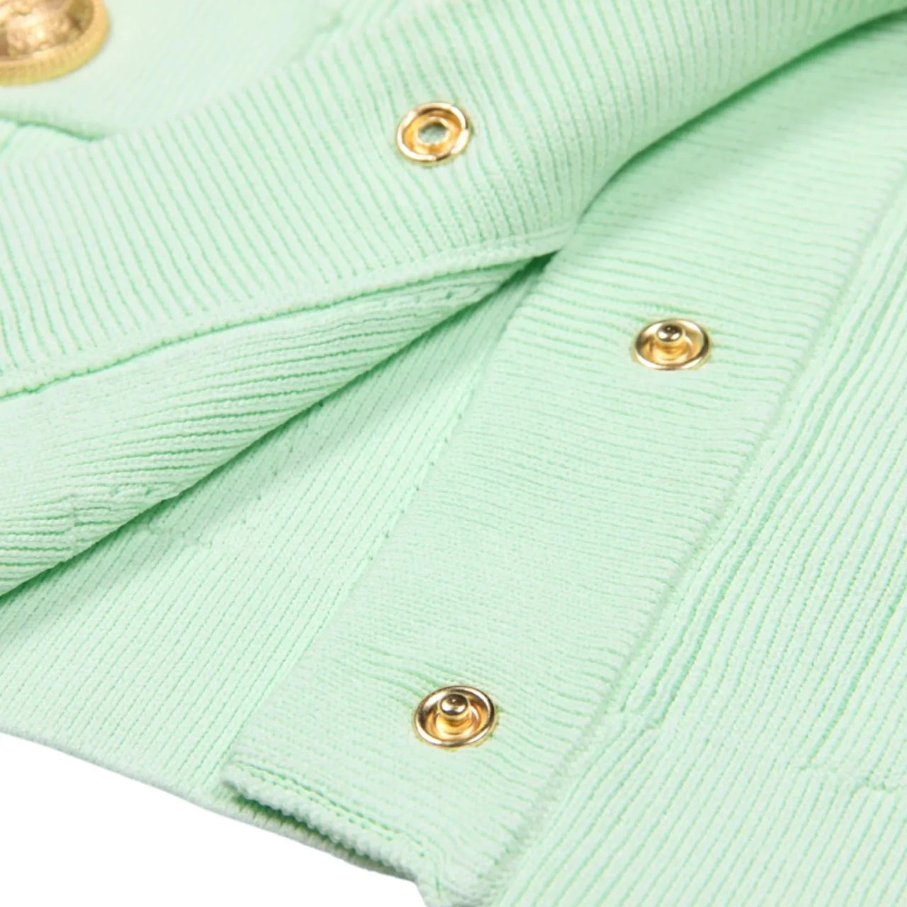 Close-up of a light green fabric with gold buttons on a white background