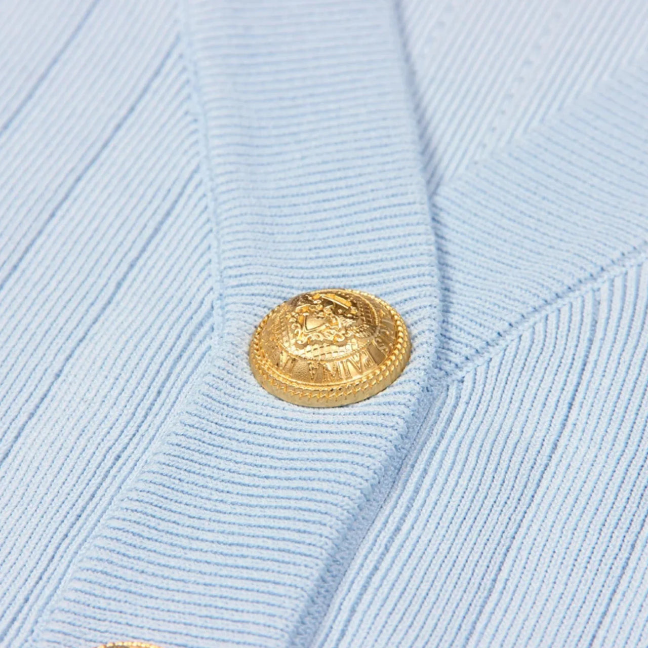 Close-up of a light blue textured fabric with a gold button.
