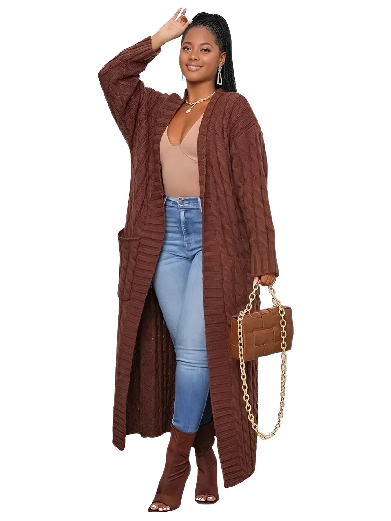 Woman wearing a long brown cardigan, beige top, blue jeans, and brown boots on a white background.
