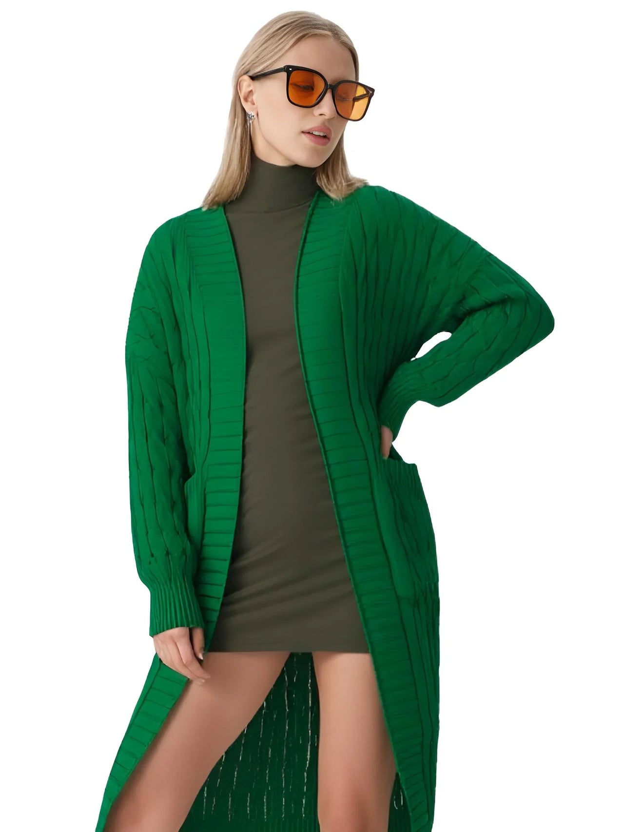 Woman wearing a long green cardigan over a green dress with sunglasses on a white background