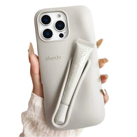 Thumbnail for Grey silicone lipstick iPhone case with a matching lip gloss attached, branded 'rhode', held by a hand.