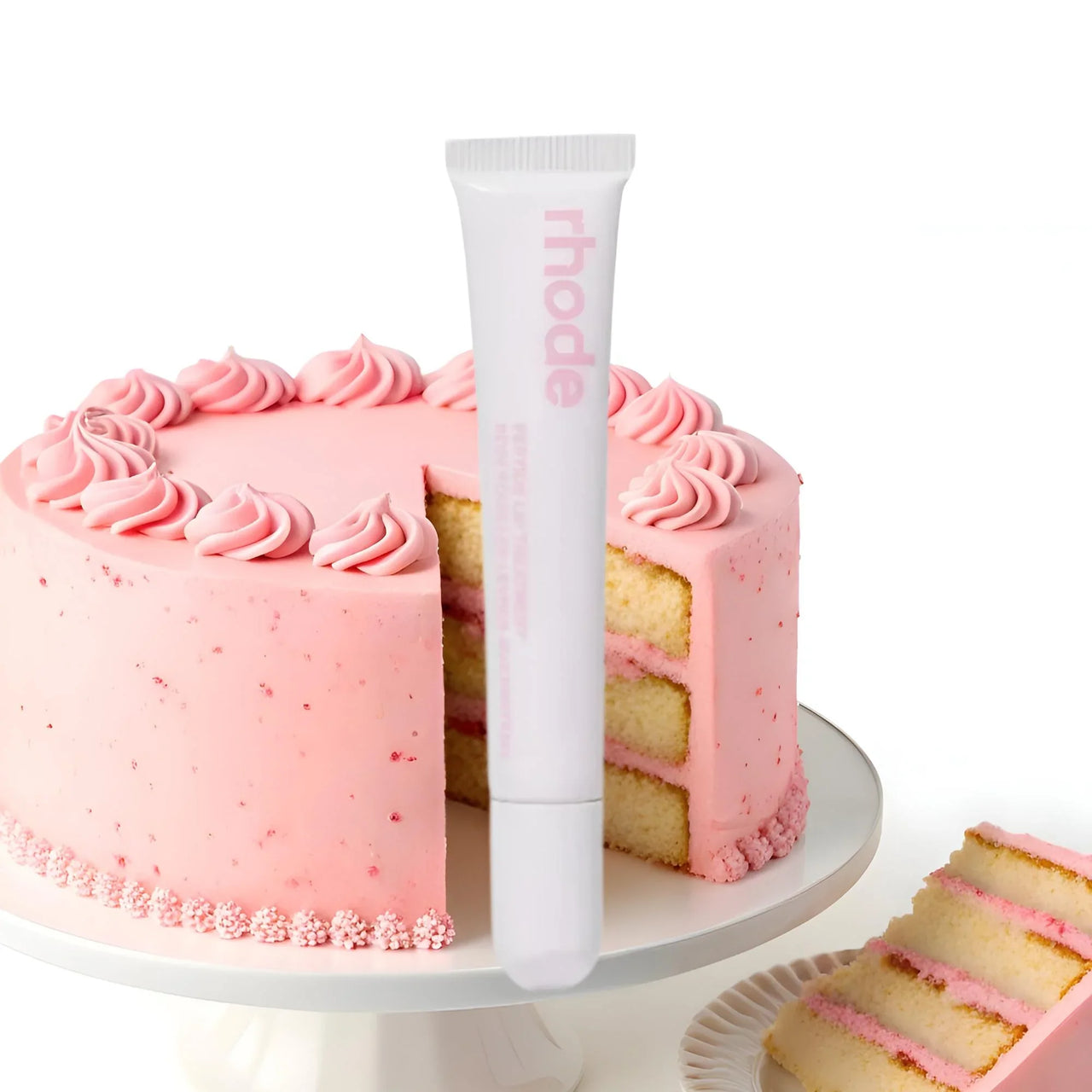 Pink frosted cake with a tube of 'rhode' vanilla cake lipgloss on a white background