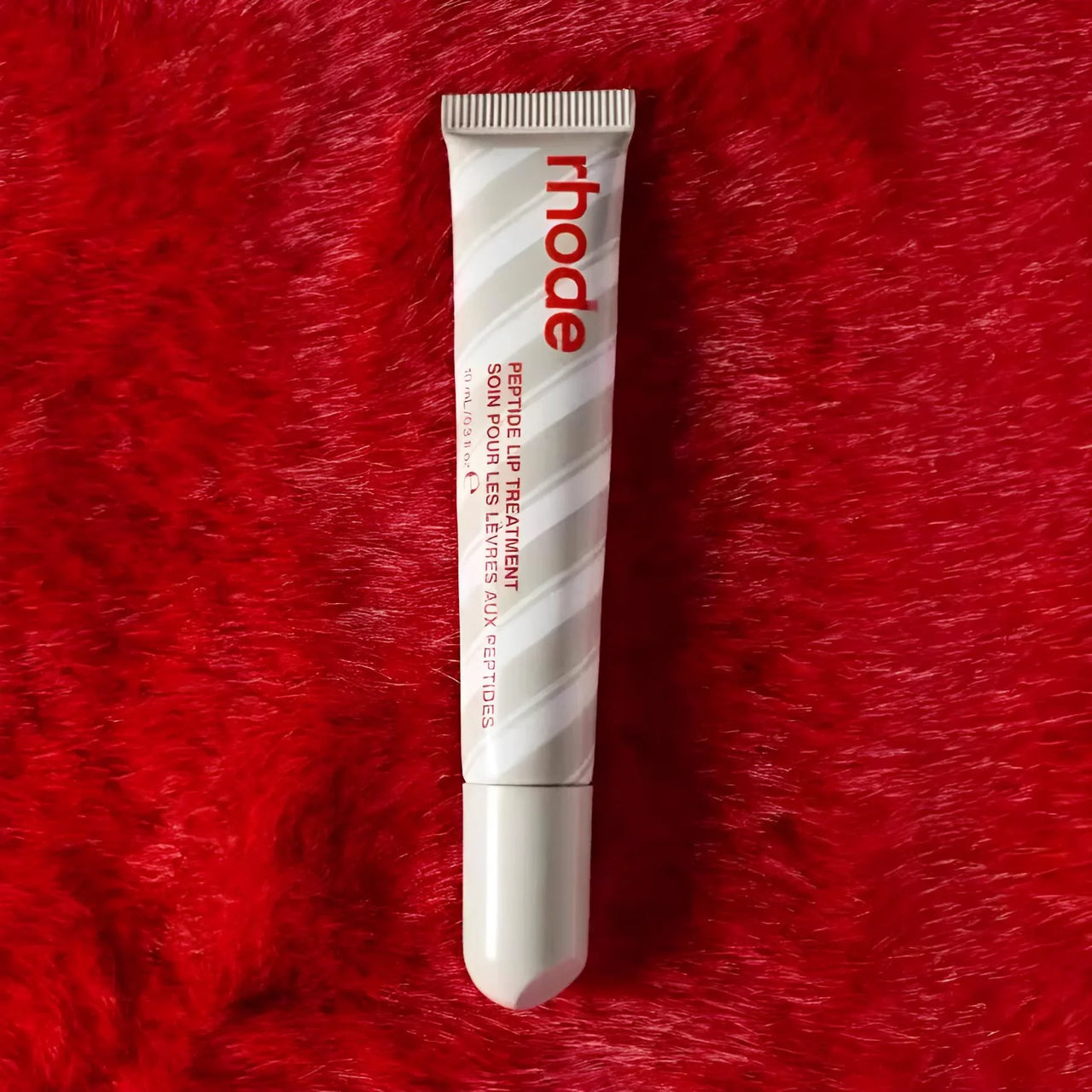 Tube of 'rhode' peppermint glaze lip balm on a red textured background