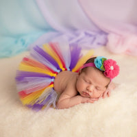 Thumbnail for Newborn baby wearing a colorful tutu and headband on a soft surface with a pastel background