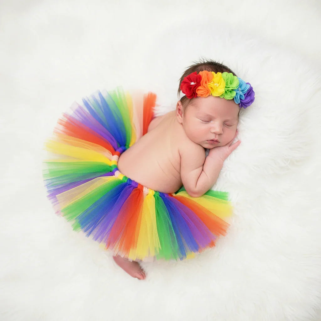 Newborn baby wearing a rainbow tutu and headband on a white background