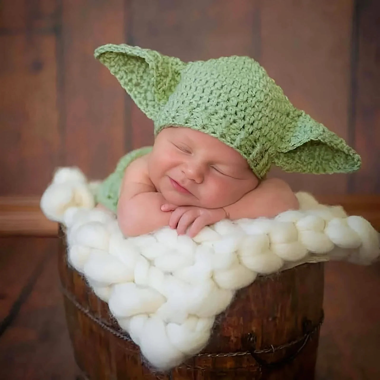 Newborn baby wearing a green Yoda hat on a wooden surface