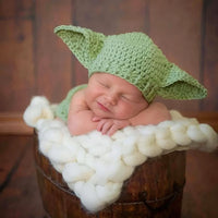 Thumbnail for Newborn baby wearing a green Yoda hat on a wooden surface