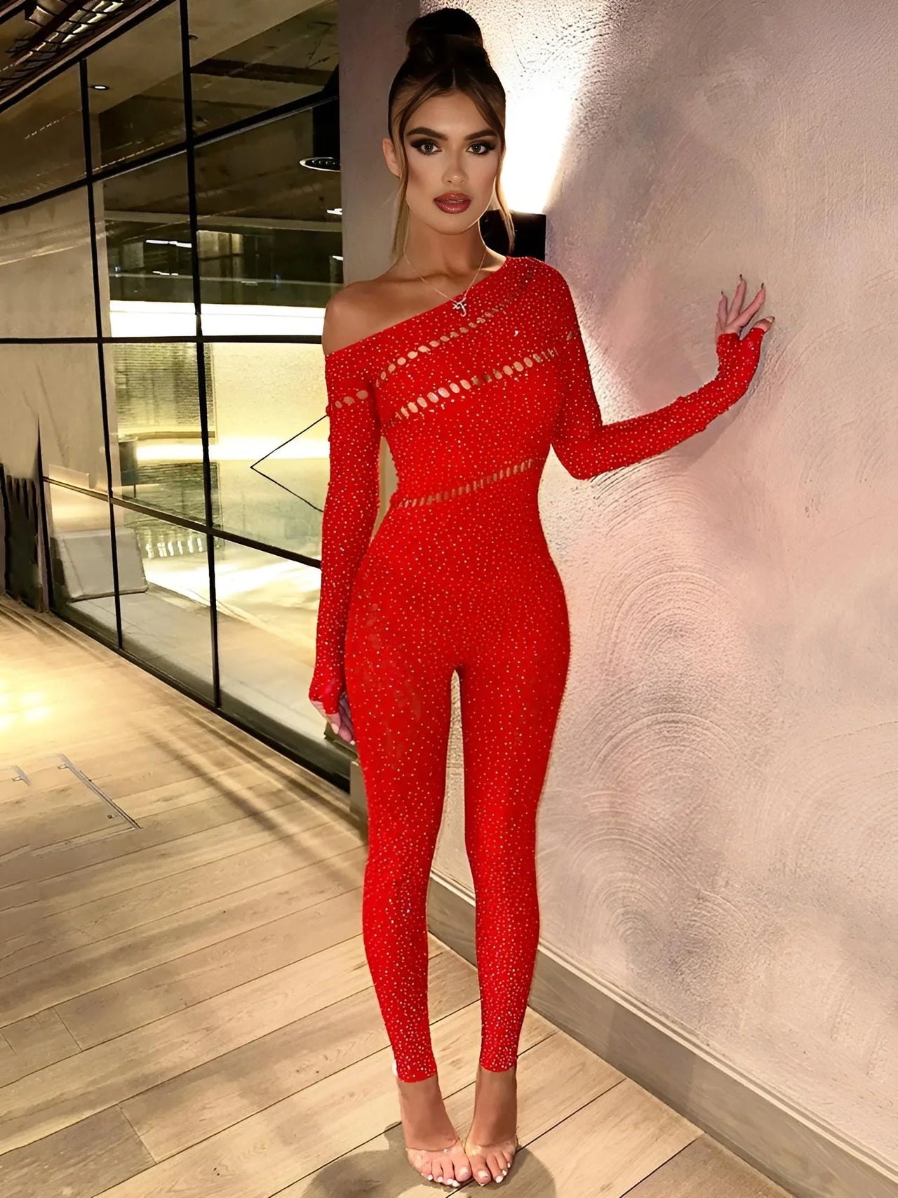 Woman wearing a red, sparkly jumpsuit standing against a textured wall.