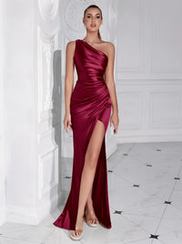 Thumbnail for Woman wearing a burgundy one shoulder maxi dress with a high slit in a white room.