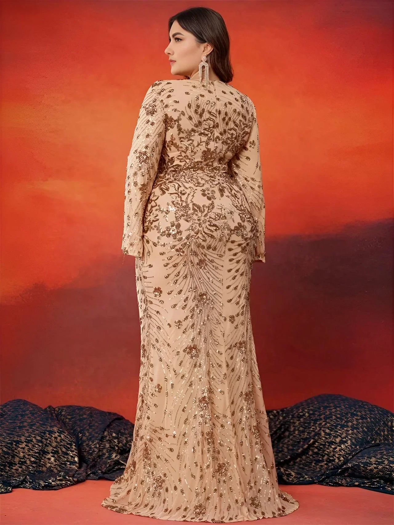 Woman in a plus size formal dress posing against an orange and red gradient background