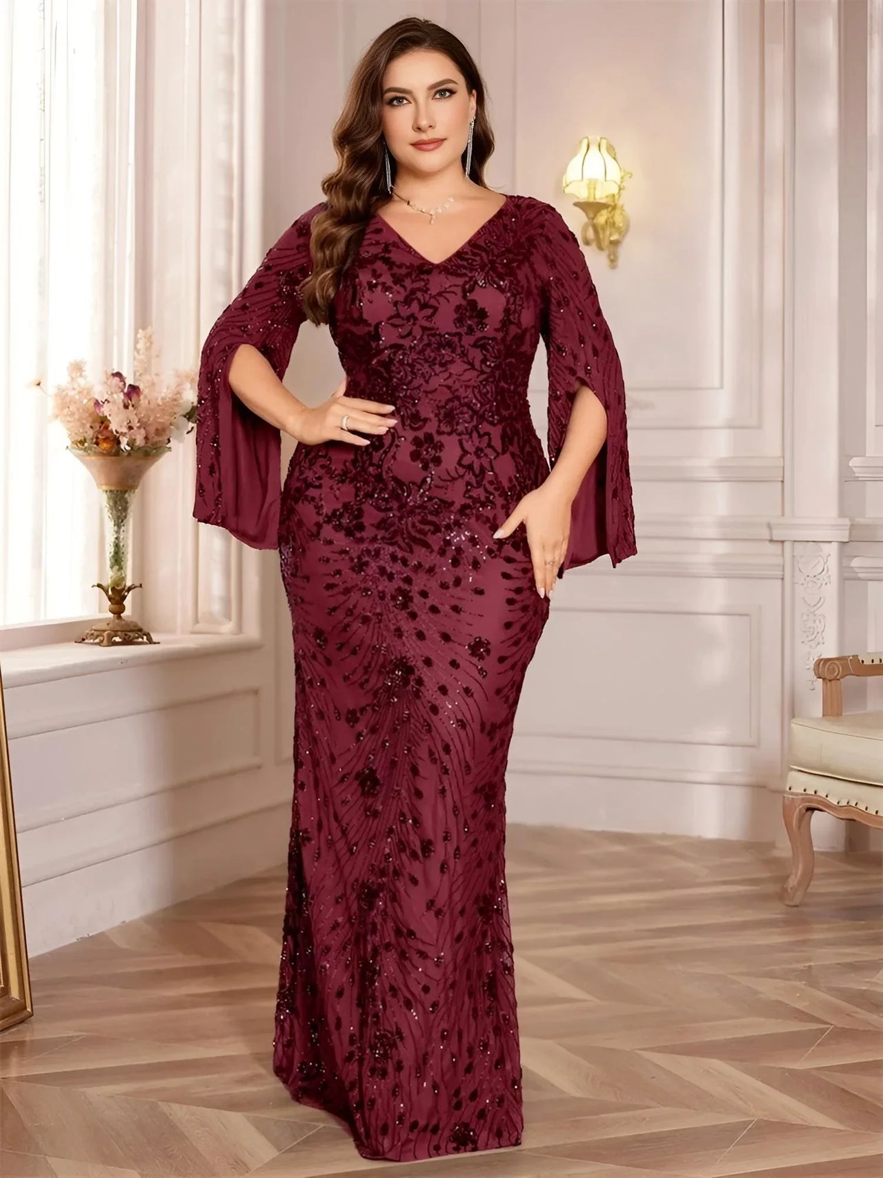 Plus size woman wearing a burgundy evening gown with floral lace details in an elegant room.