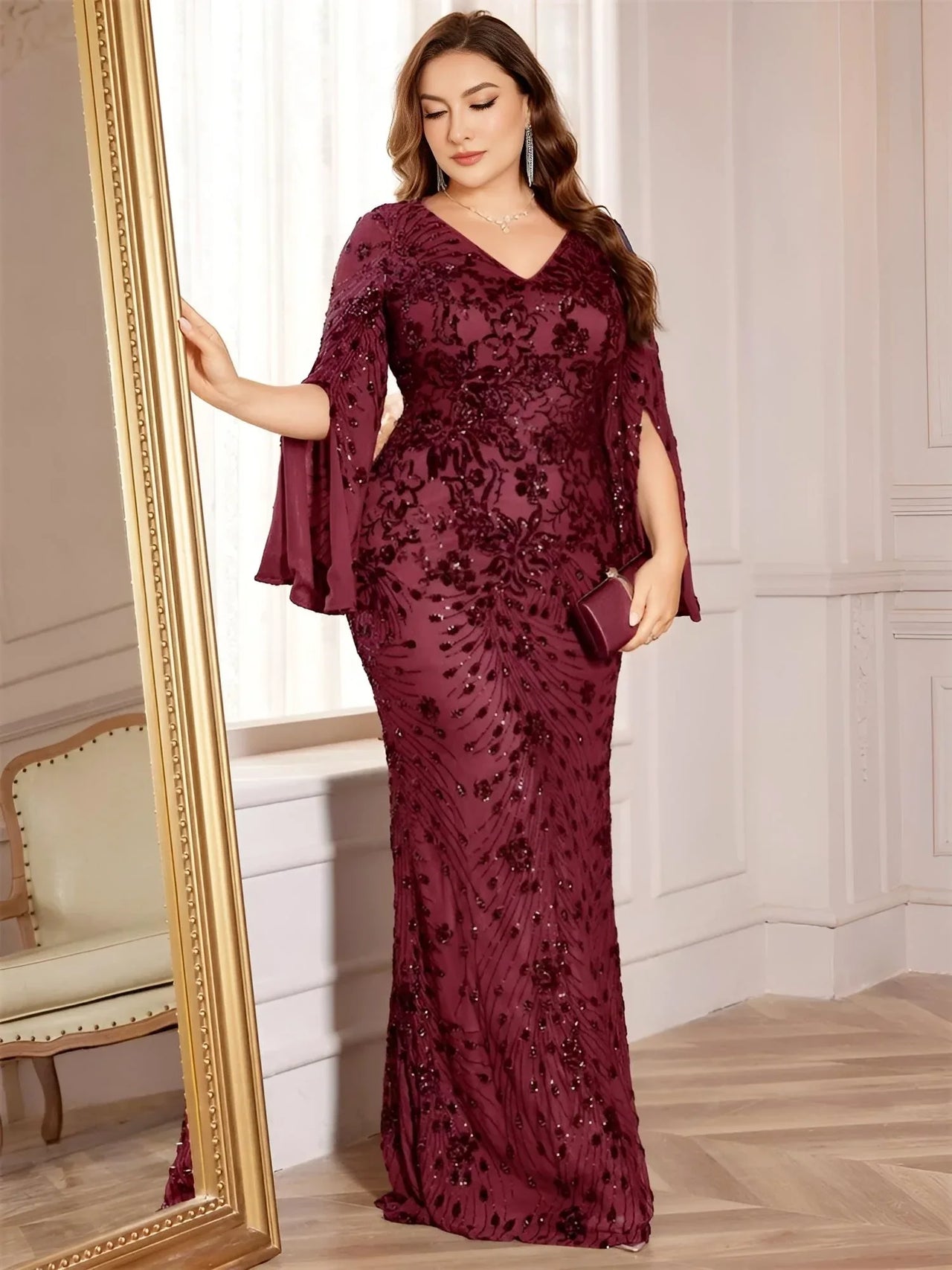 Plus size woman wearing a burgundy evening gown with floral lace details in an elegant room.