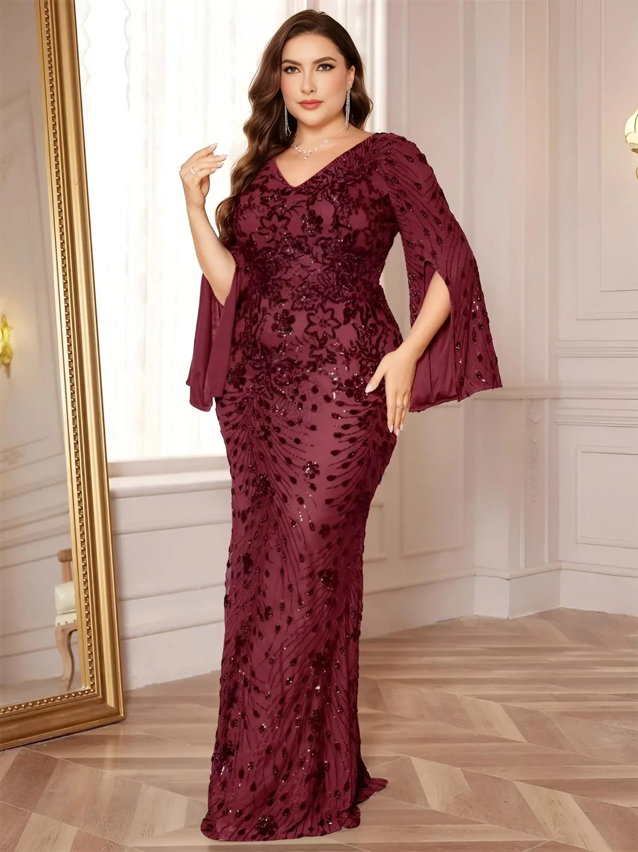 Woman wearing a plus size burgundy evening gown with floral patterns in a room with a mirror and wooden floor.