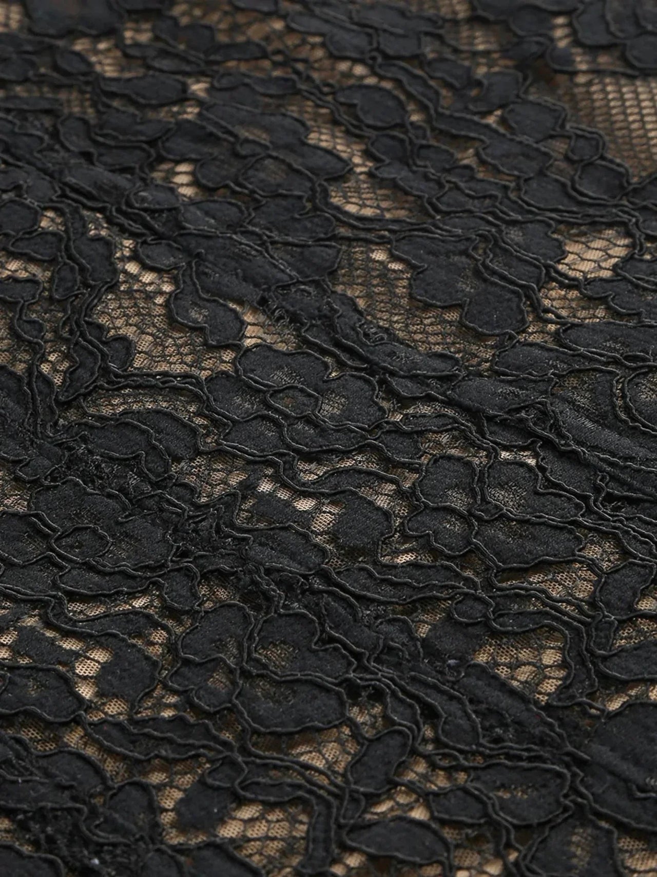 Close-up of black sheer lace dress fabric with intricate floral pattern on a white background