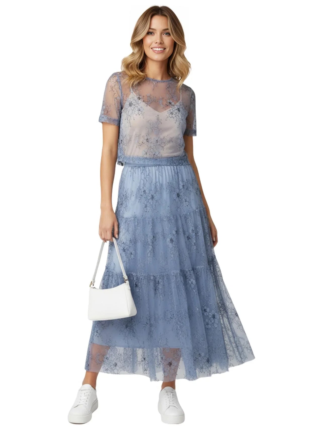 Woman wearing a blue lace maxi skirt holding a white handbag on a white background