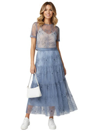 Thumbnail for Woman wearing a blue lace maxi skirt holding a white handbag on a white background