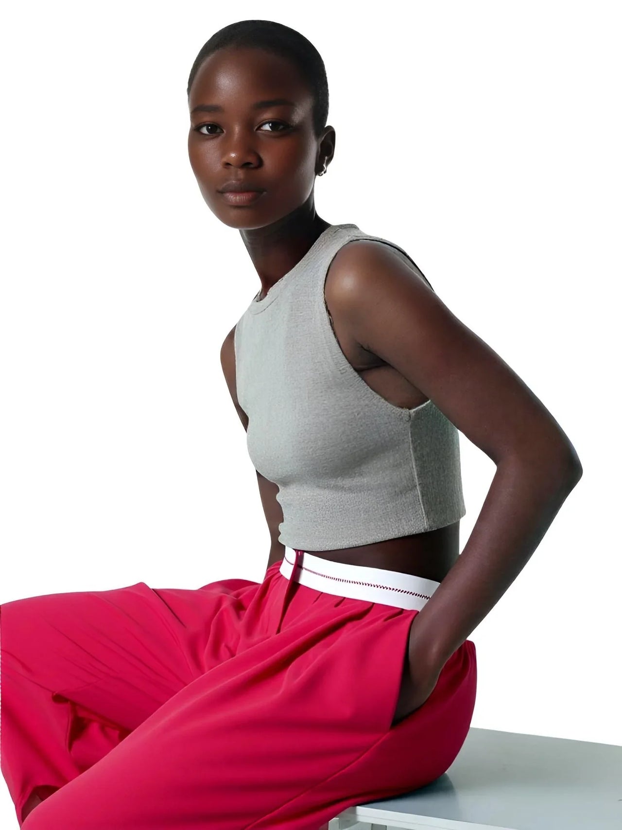 Woman wearing a gray crop top and red pants sitting on a white surface with a white background