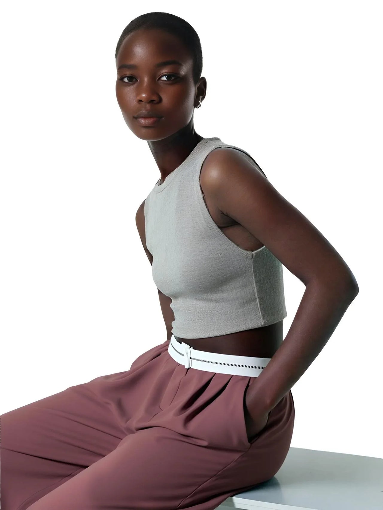 Woman wearing a gray sleeveless top and maroon pants with a white belt on a white background