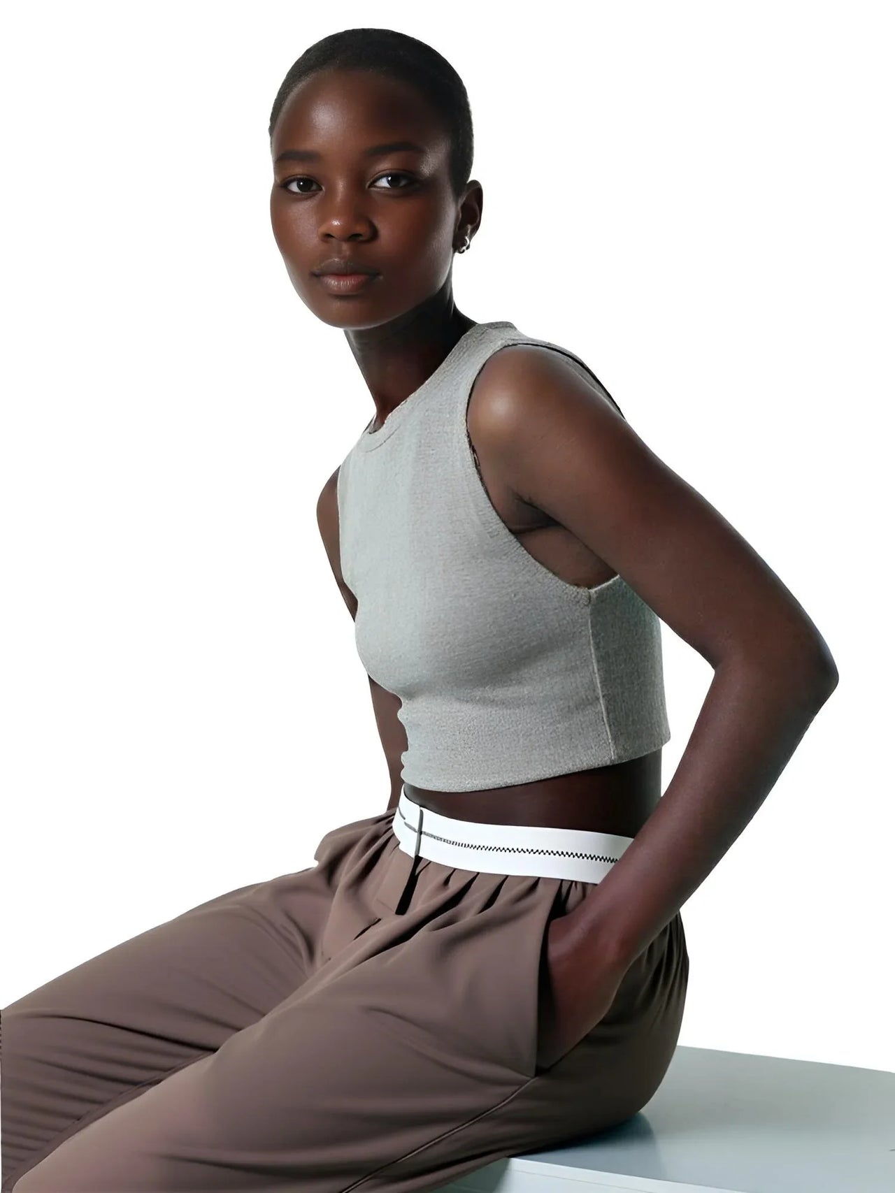 Woman wearing a gray sleeveless top and brown pants on a white background