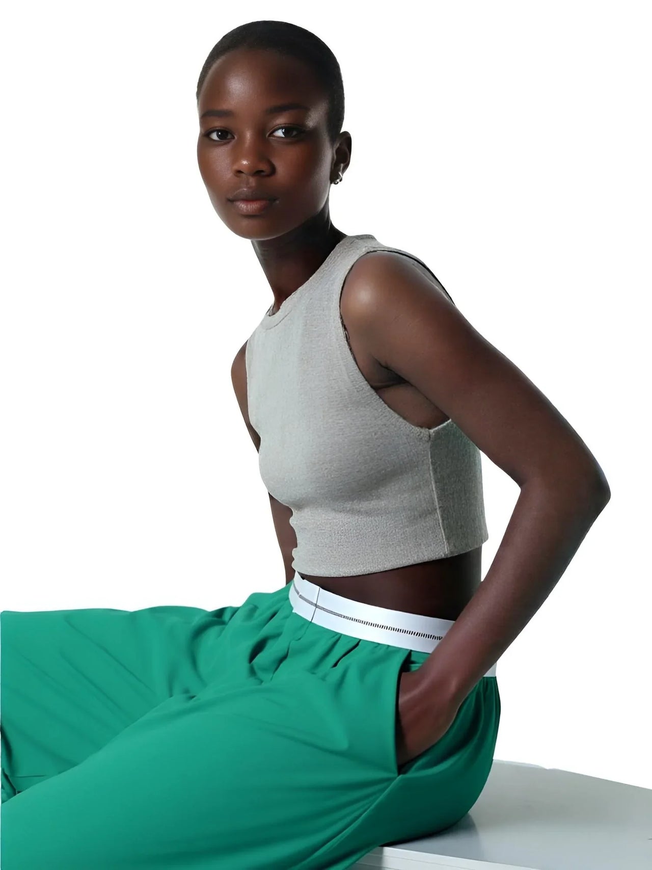 Woman wearing a gray sleeveless top and green pants on a white background