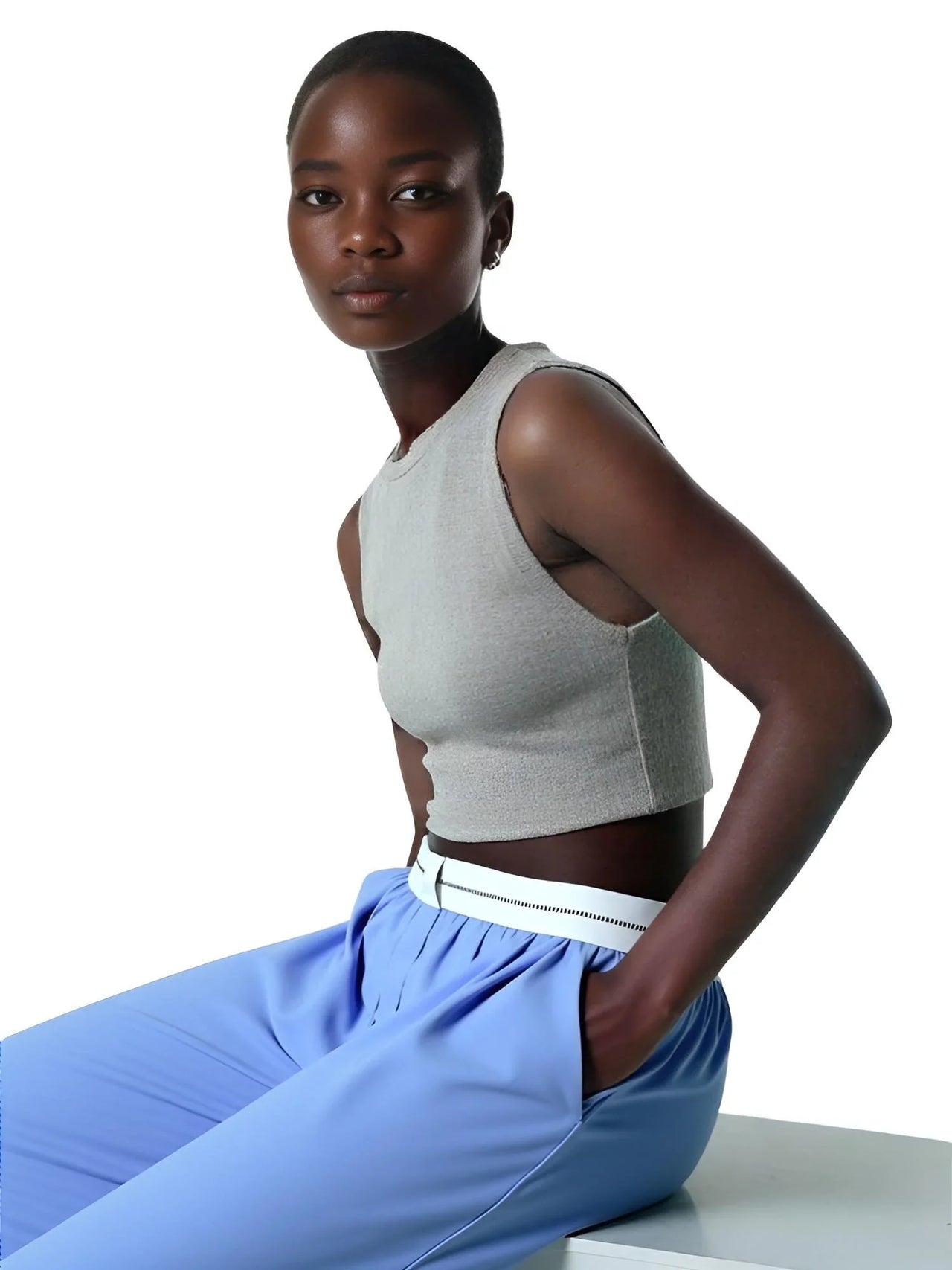 Woman wearing a gray sleeveless top and blue pants on a white background