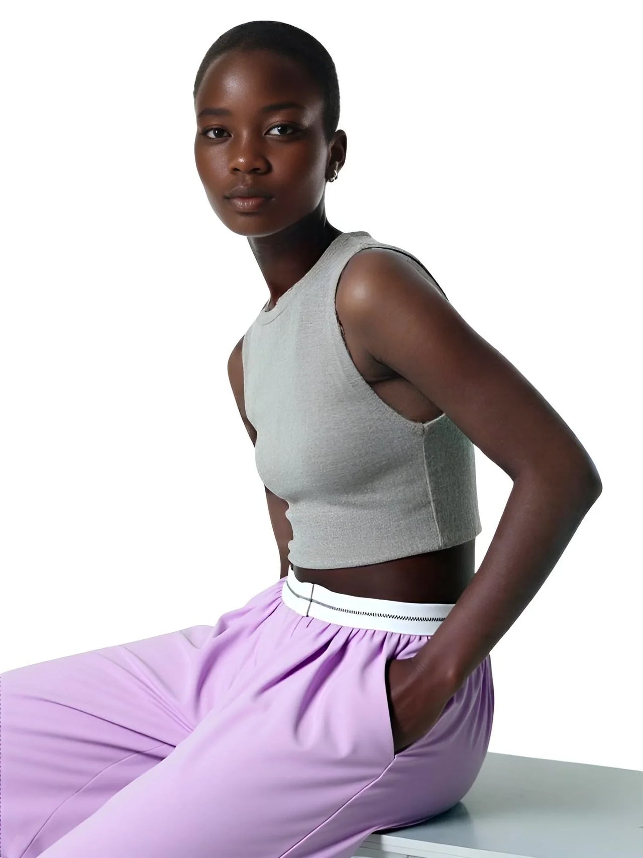 Woman wearing a gray crop top and purple pants on a white background