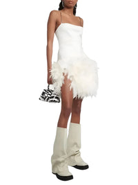 Thumbnail for Woman wearing a white dress with feather details and white knee high slouch boots on a white background