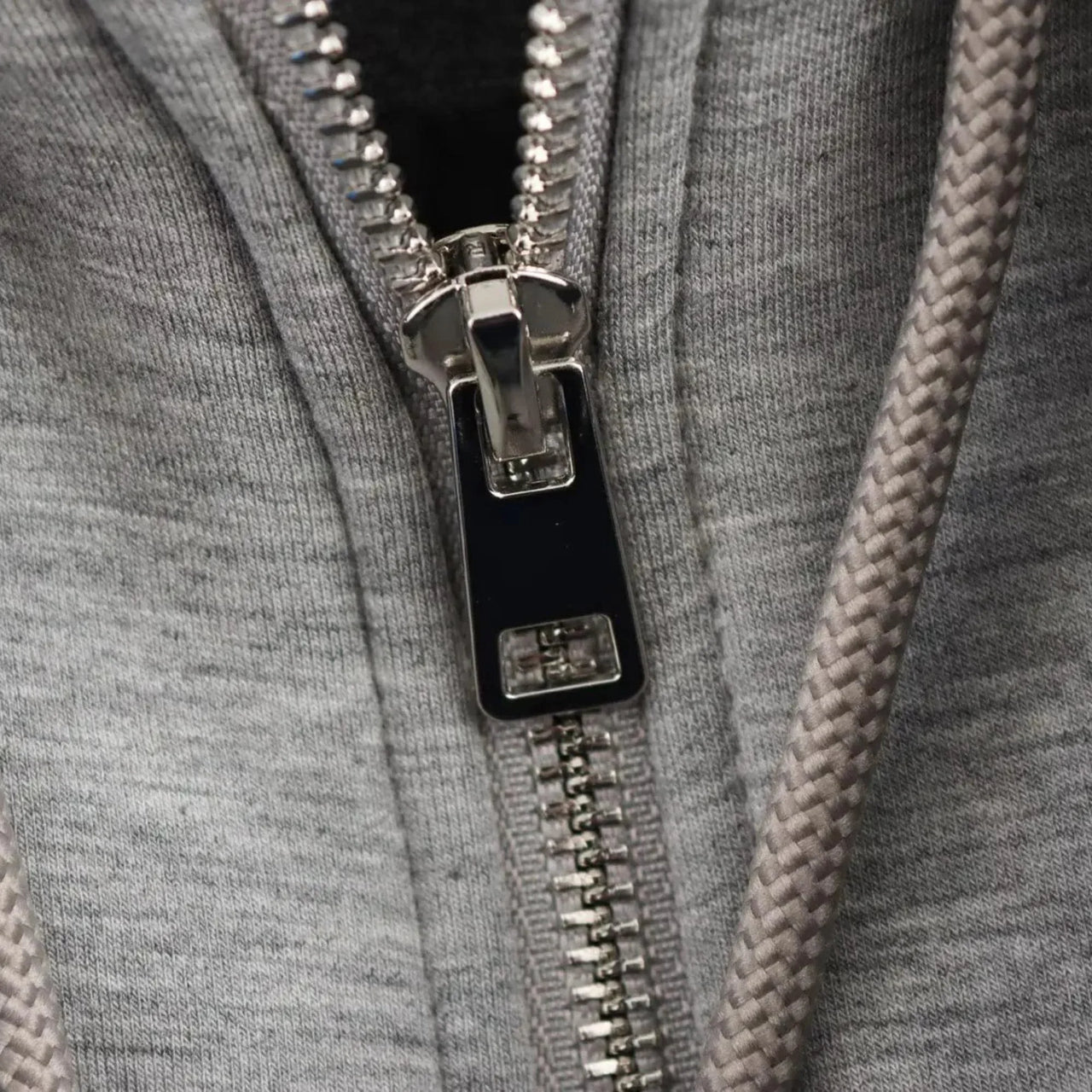 Close-up of a zipper on a gray garment with a braided texture.