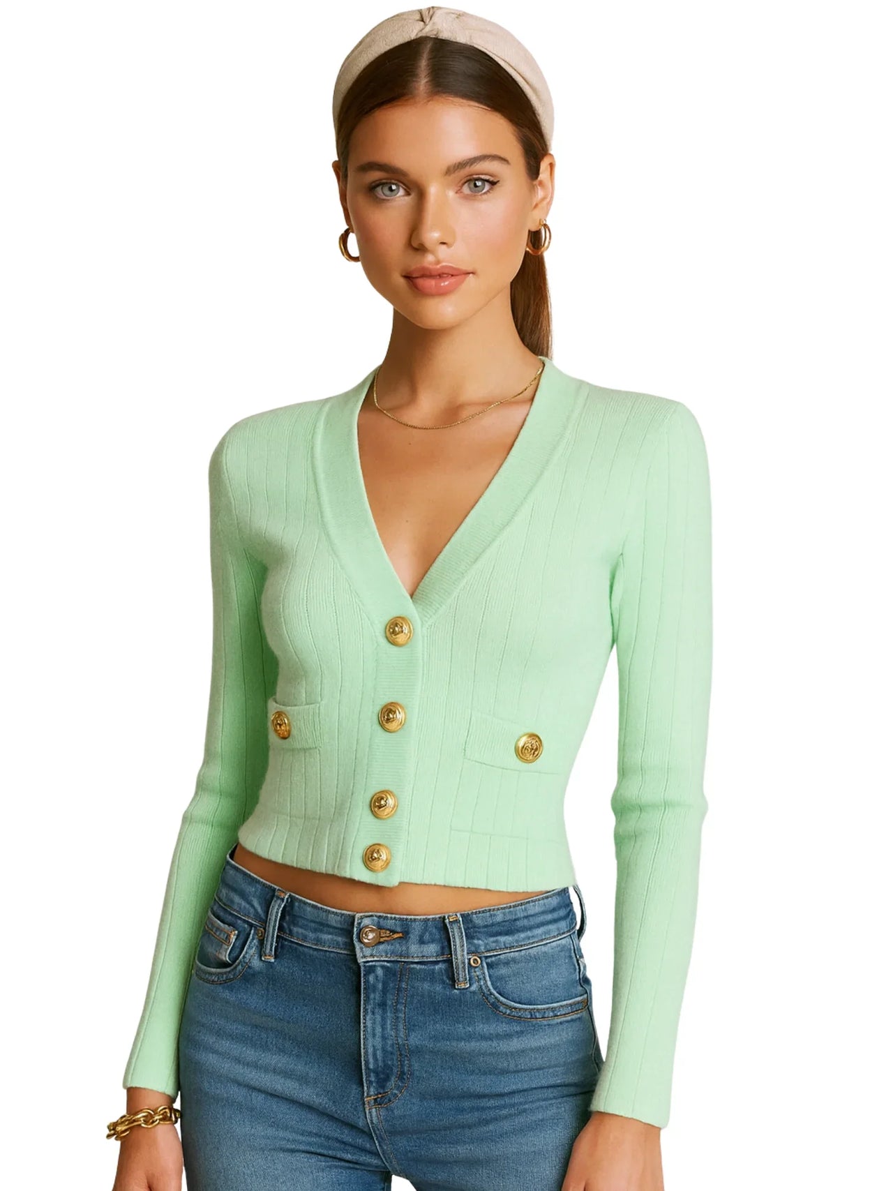Woman wearing a light green cardigan with gold buttons and blue jeans on a white background