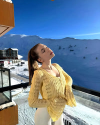 Thumbnail for Woman in a yellow cardigan standing on a balcony with a snowy mountain landscape in the background