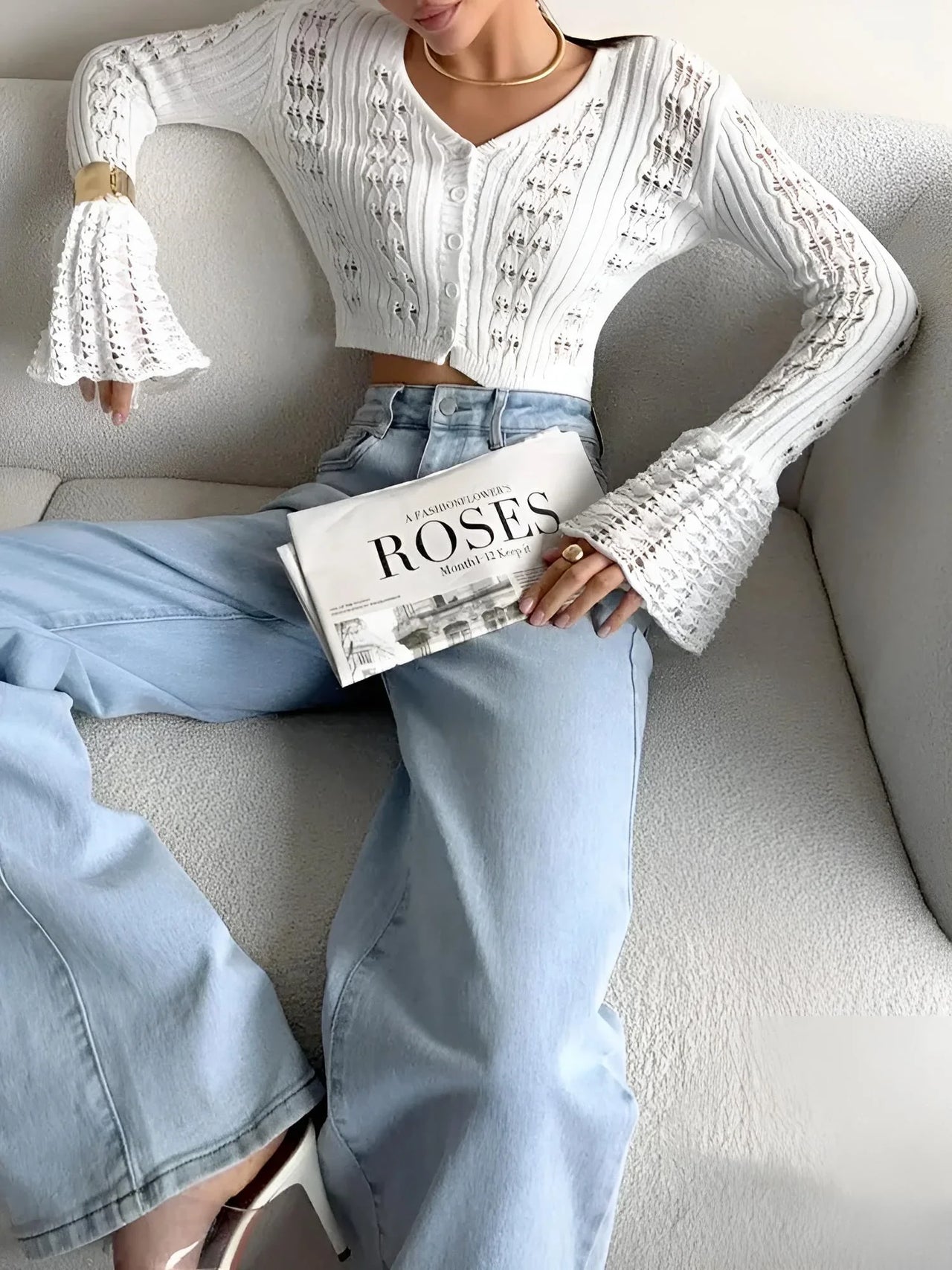 Person wearing a white long sleeve top and light blue jeans, holding a book titled 'Roses', sitting on a gray couch.