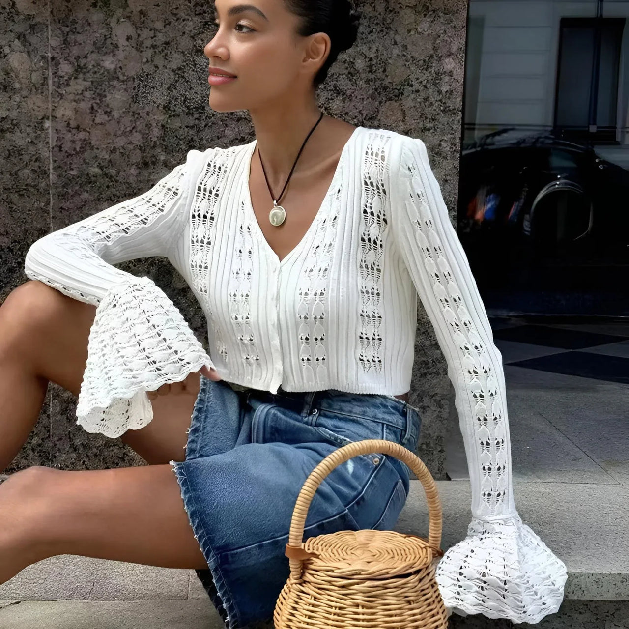 Woman wearing a white flare sleeve cardigan and denim shorts, sitting on steps with a woven basket.