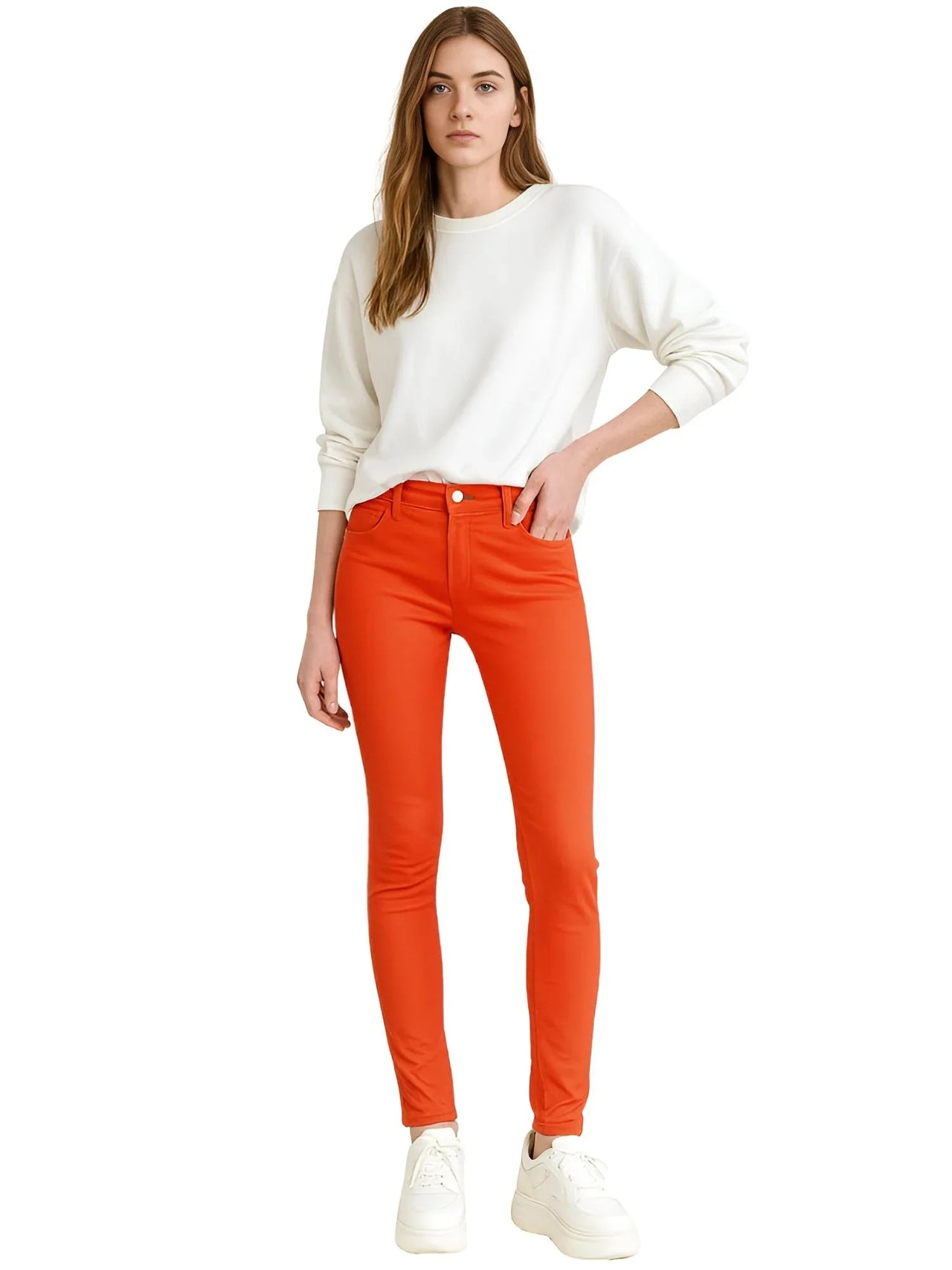 Woman wearing a white sweater and bright orange skinny jeans on a white background