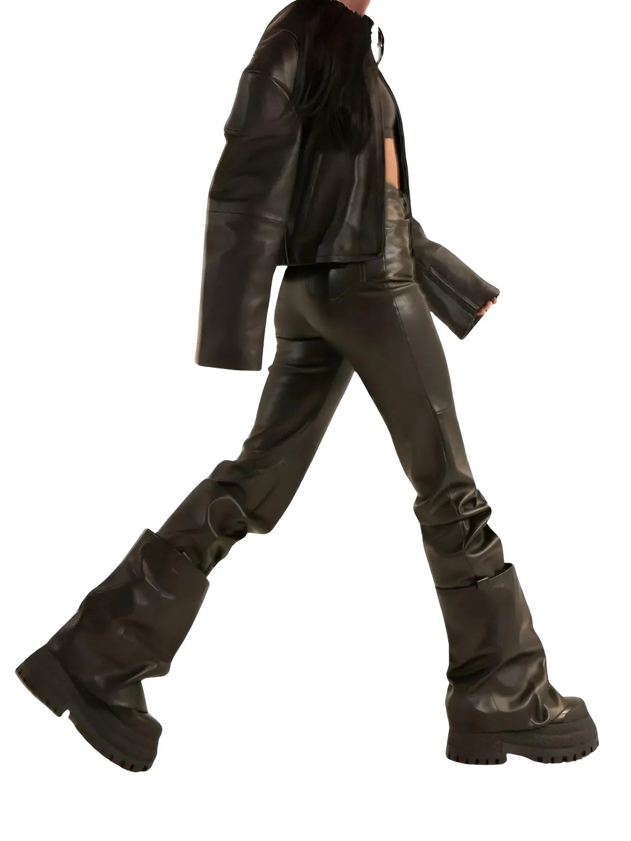Woman wearing a black leather jacket and pants and brown leather platform slouch boots on a white background