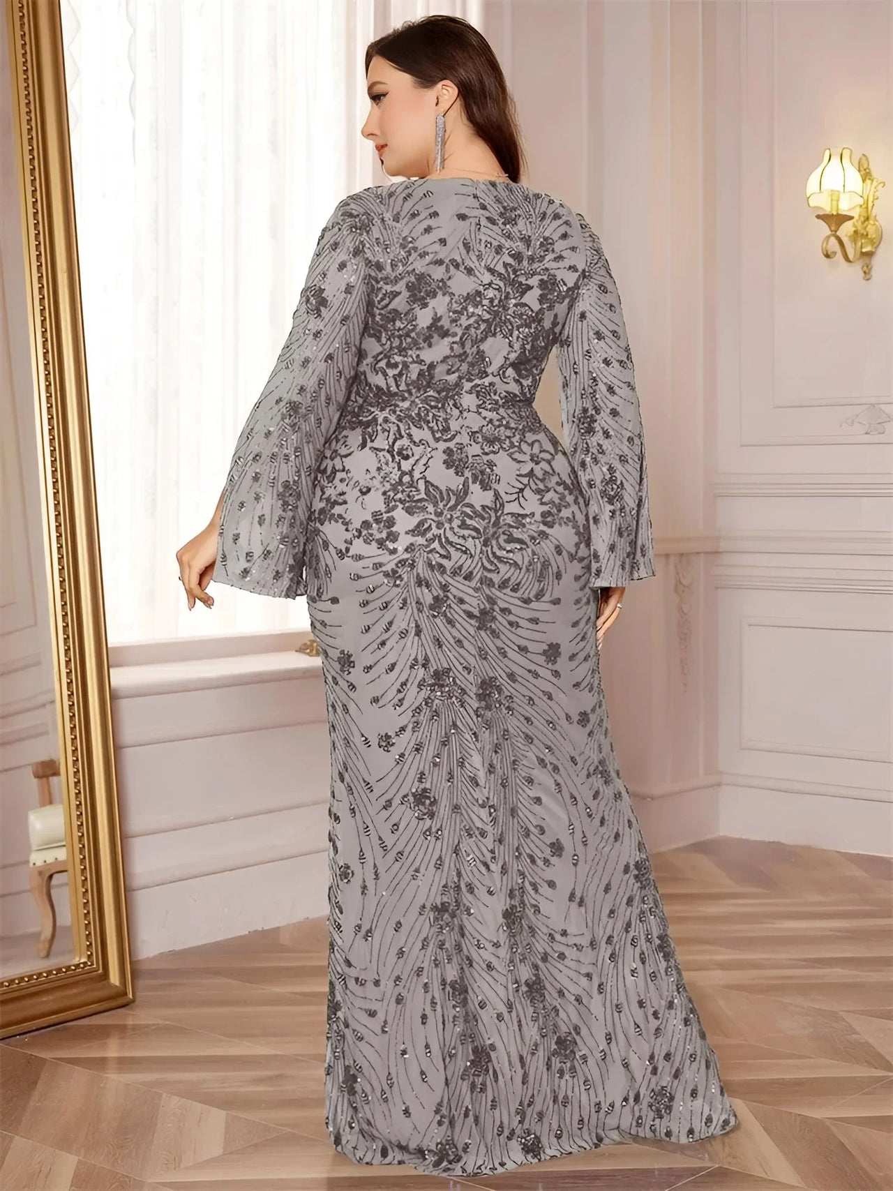 Woman wearing a gray floral maxi dress in an elegant room with a mirror and light fixture.
