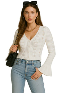 Thumbnail for Woman wearing a white flare sleeve cardigan sweater and blue jeans, holding a black handbag.