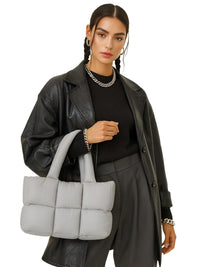 Thumbnail for Woman holding a gray puffer bag against a white background