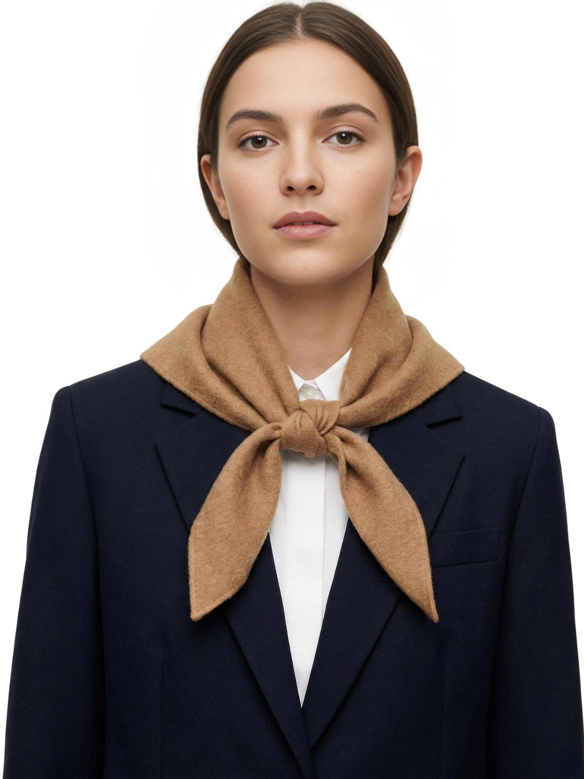 Woman wearing a camel colored wool scarf and navy blazer on a white background