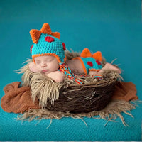 Thumbnail for Newborn baby wearing a dinosaur-themed crochet hat and outfit, lying in a nest on a blue background.