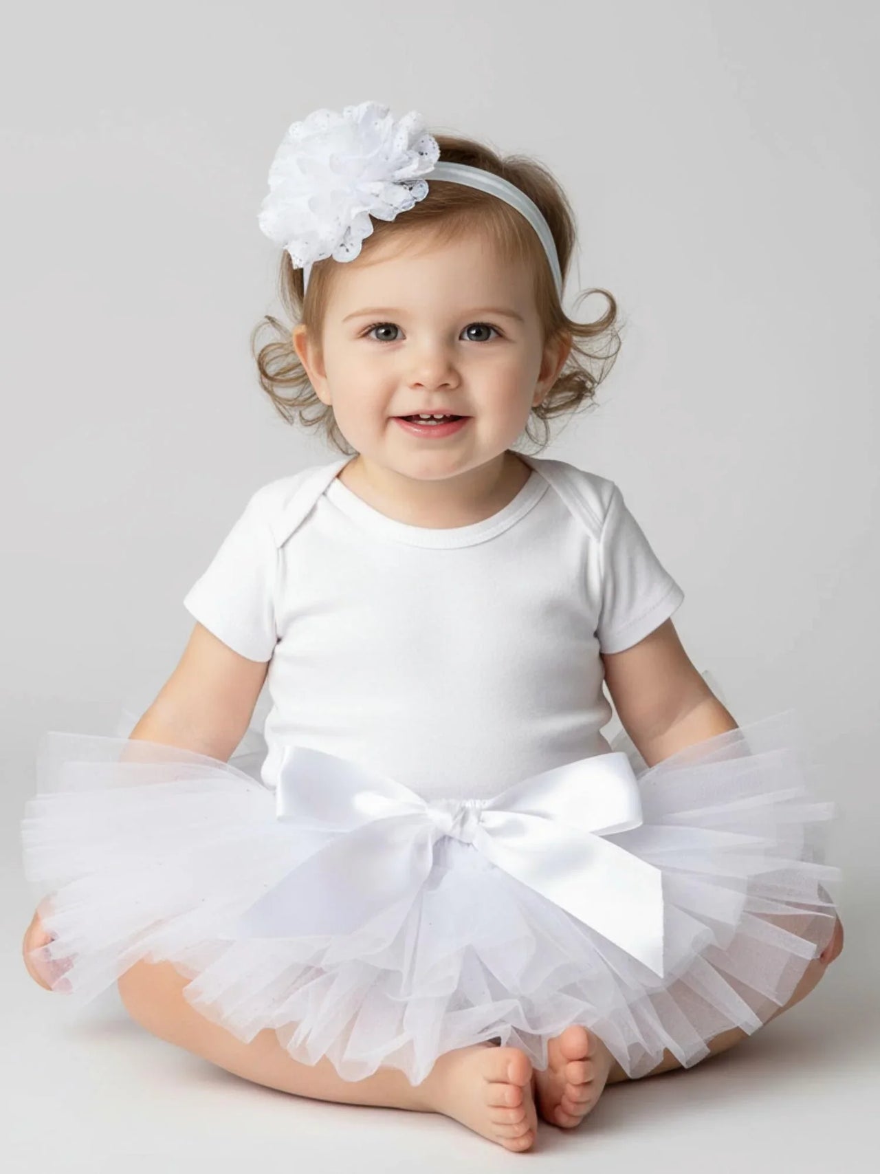 Baby wearing a white tutu and headband on a light gray background