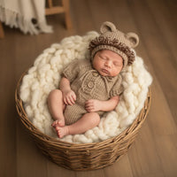 Thumbnail for Newborn baby in a knitted outfit and hat lying in a wicker basket on a wooden floor.